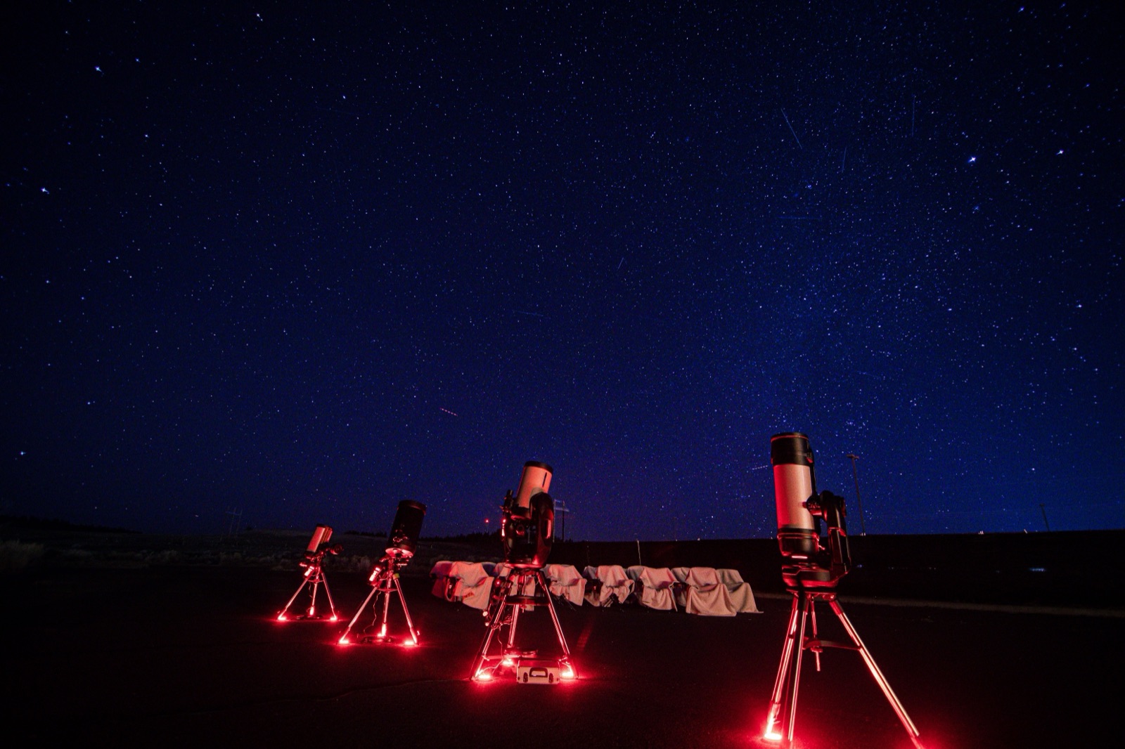Four telescopes set up under a starry sky, lit by night-vision-safe red lighting on a guided tour