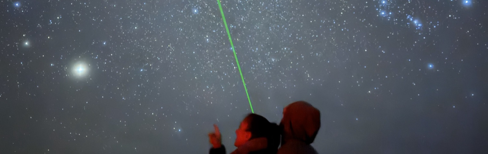 Tour guests under a dense starfield as a guide traces constellations with a green laser pointer
